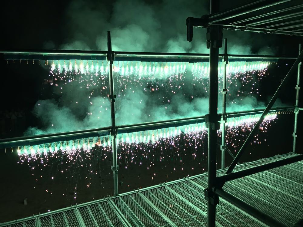 足場に吊るされた仕掛け花火が夜に燃える様子